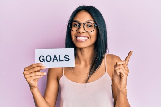 A woman holding a sign that reads “GOALS” and pointing upwards.