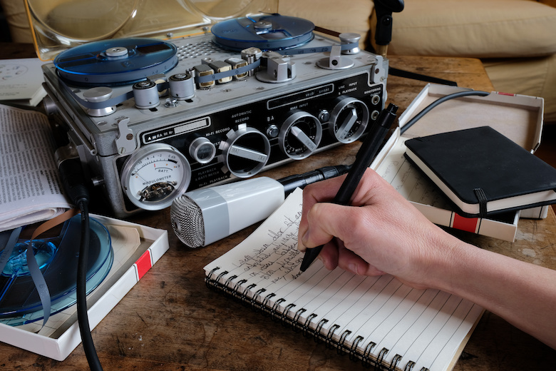 A photo of a vintage boombox and a hand writing in a notebook on a wooden table. A photo of a vintage boombox and a hand writing in a notebook on a wooden table.