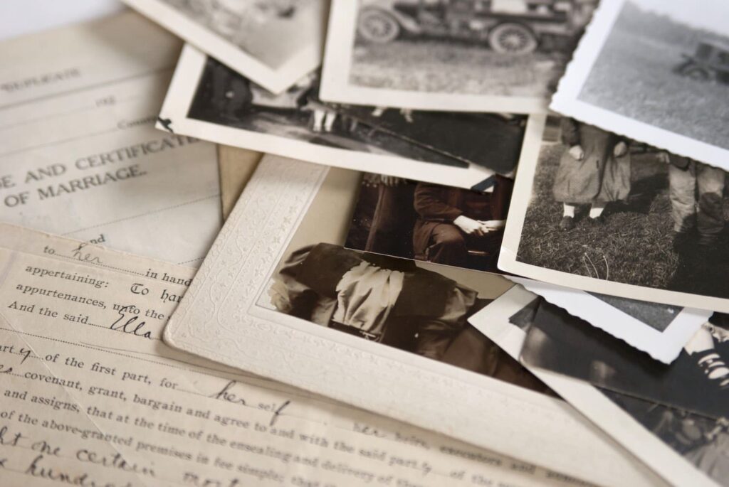 Family Storytelling A collection of old black and white photographs and a marriage certificate on a wooden table with a white tablecloth.